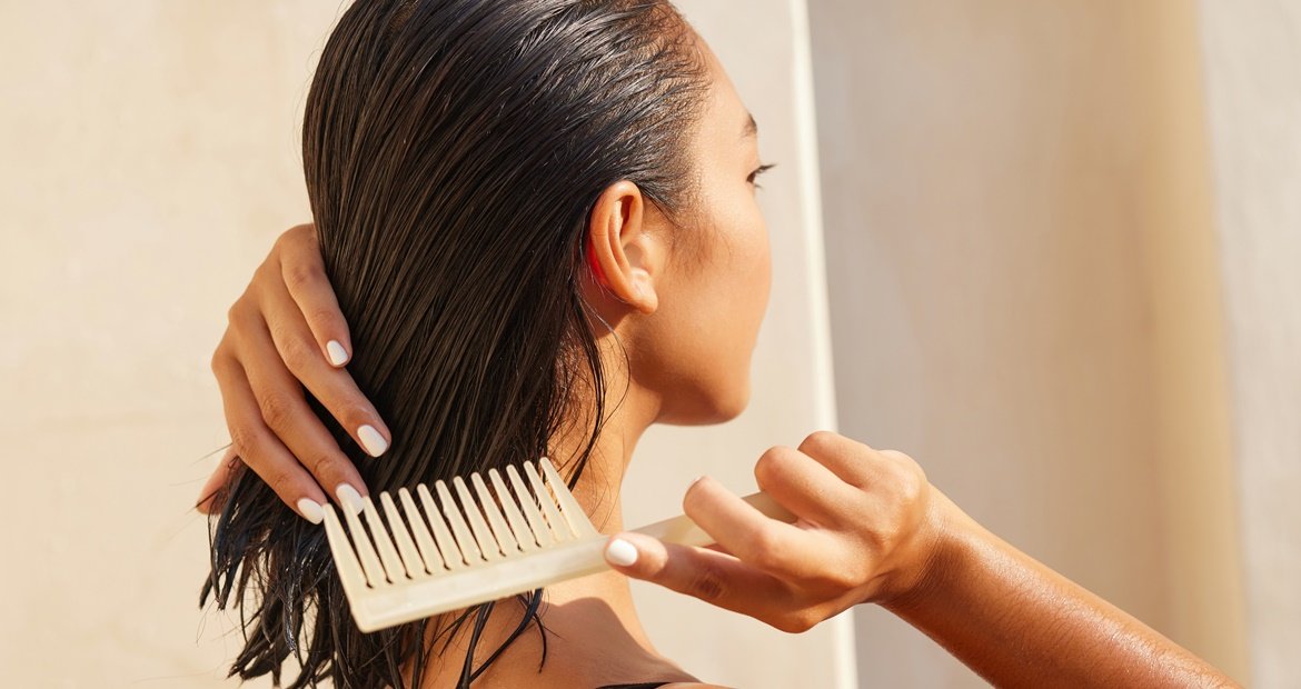 Mulher penteando o cabelo após aplicar uma grande quantidade de manteiga de karité nos fios, deixando o cabelo brilhoso.